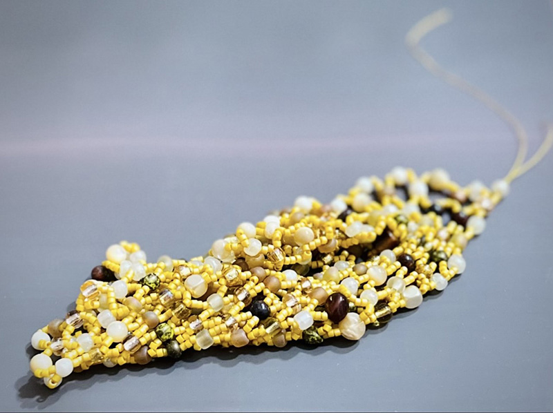 A net-like beaded structure made of yellow, black, and pearlescent beads.