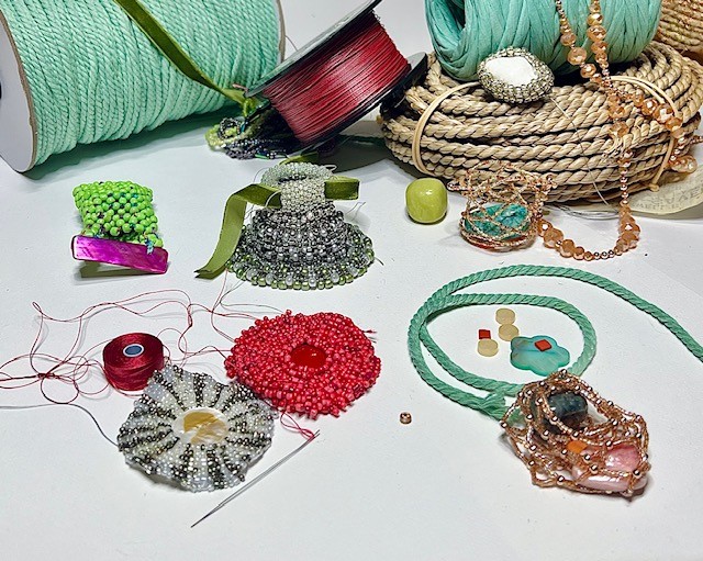 An assortment of works in progress using brightly colored beads, thread, rope, and ribbons.