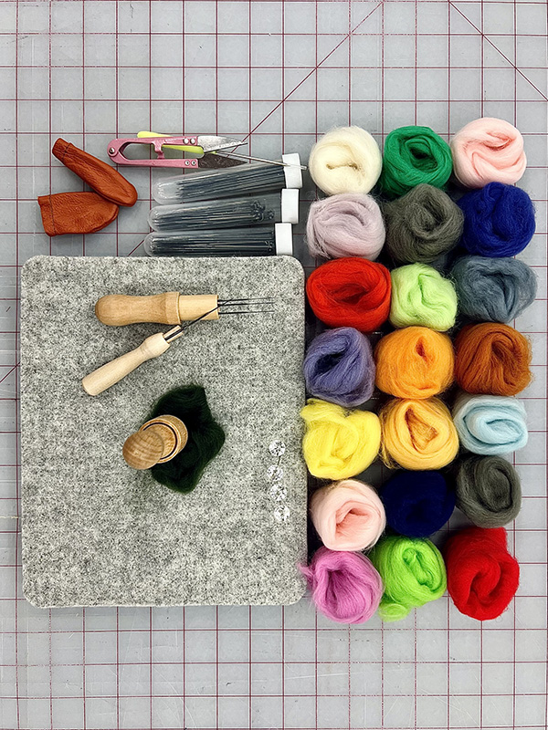 A collection of colorful wool roving with assorted needles and a blank rectangle of wool ready as a blank canvas.