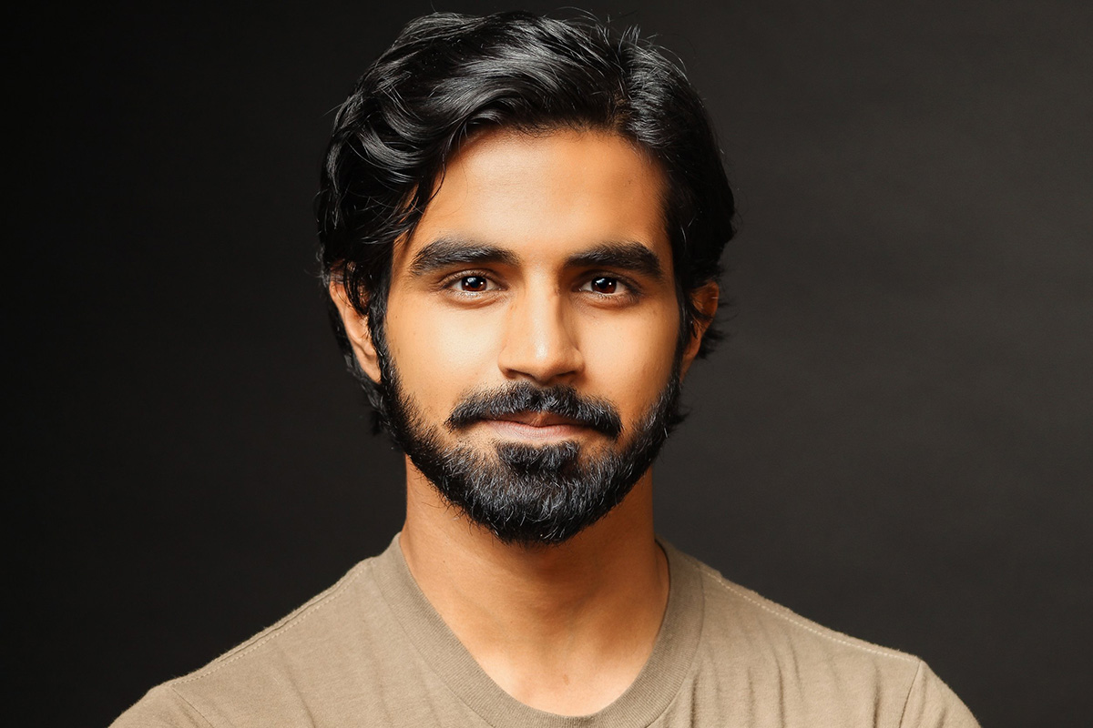 Headshot of Taha, wearing a tan tshirt against a dark background