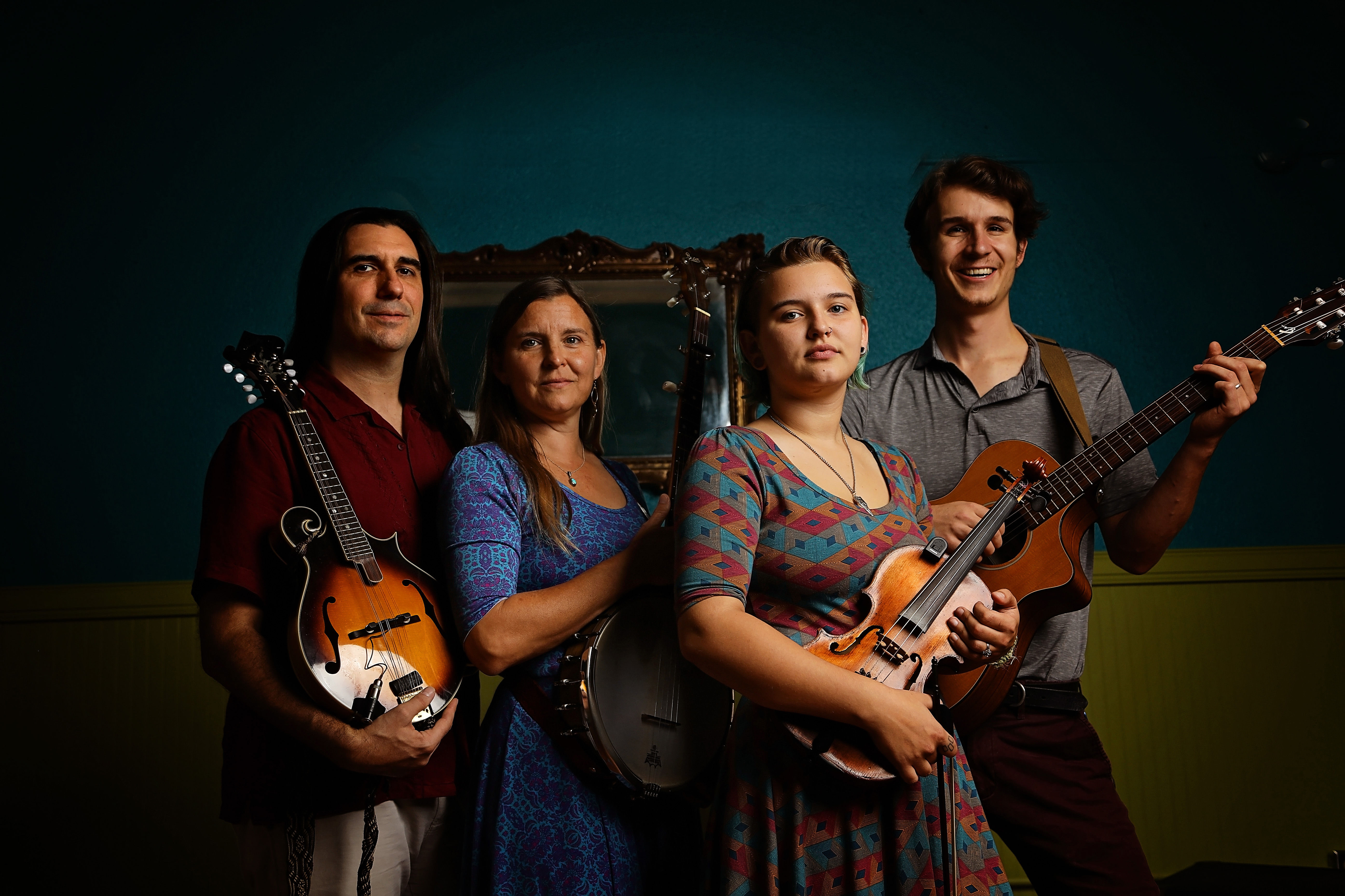 Image of four people holding bluegrass instruments, against a dark green backdrop