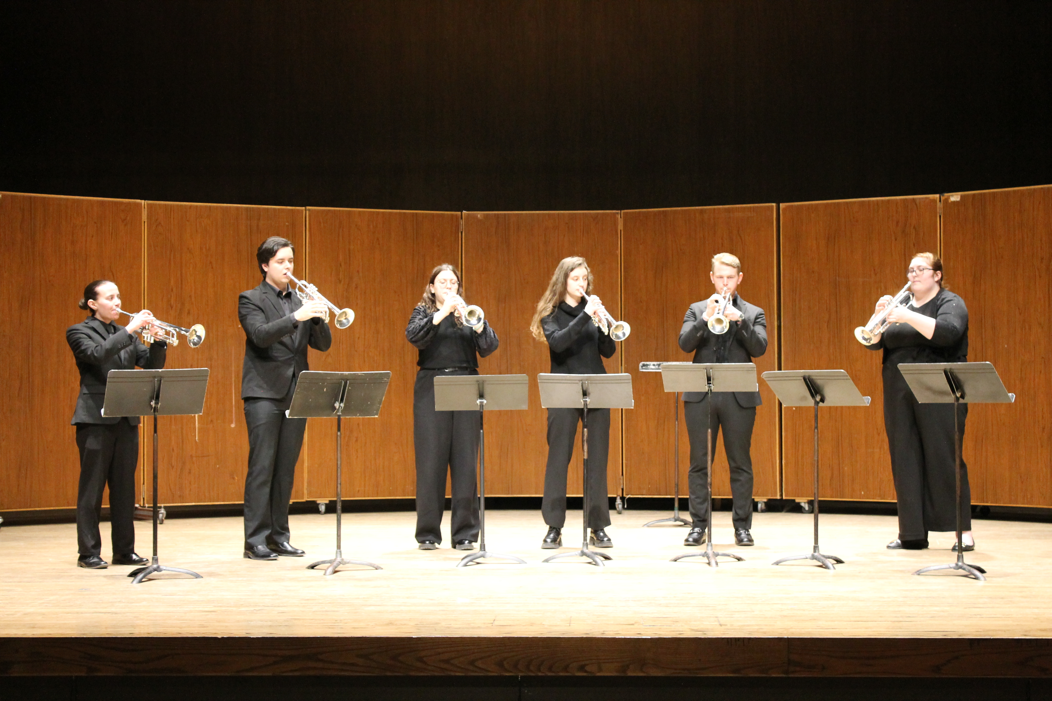 Members of the Baroque Trumpet ensemble standing onstage wearing black clothing playing their instruments behind music stands