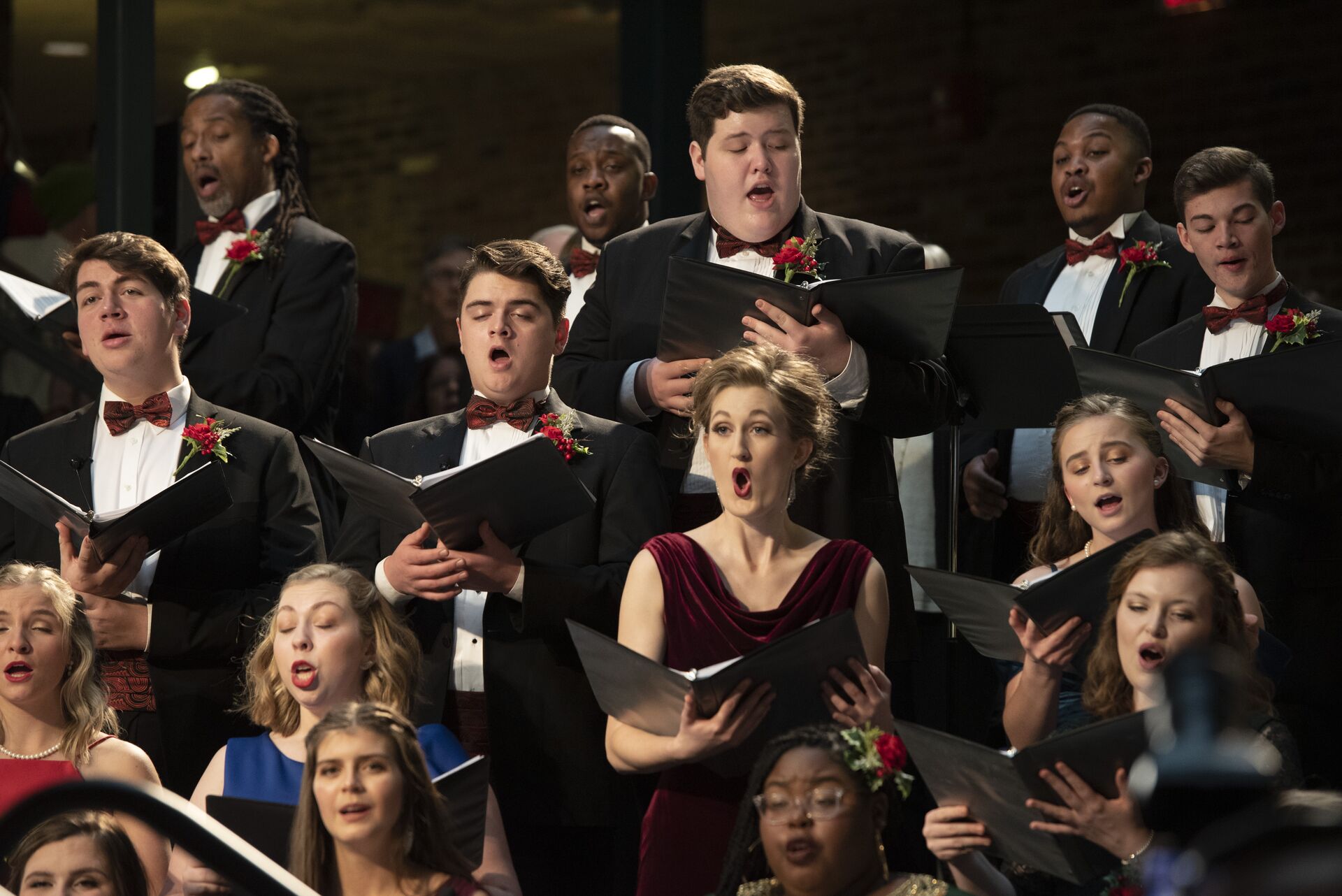 Singers wearing formal attire hold music binders while performing