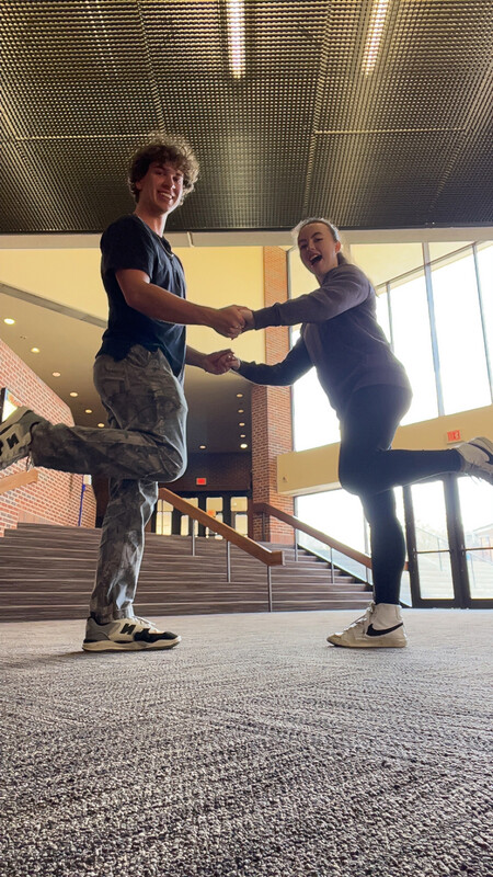 two students holding hands with their foreground leg bent upwards