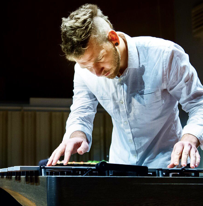Alexander Smith leans over a percussion instrument wearing a light blue button down shirt