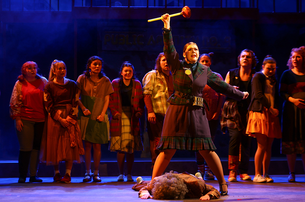 students on stage with one holding plunger in air