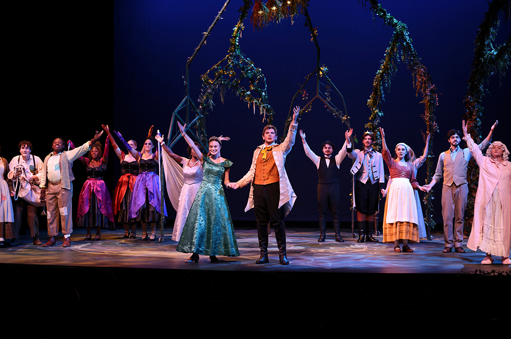 group of student actors on stage with arms up