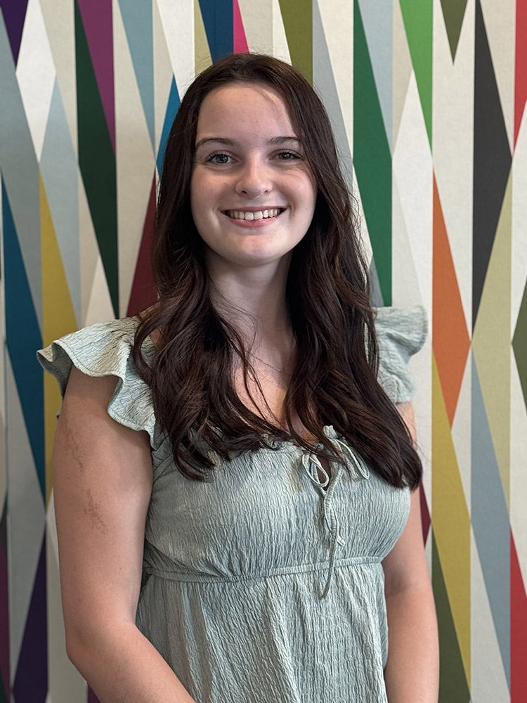 Student Ambassador Chloe Scarola stands in front of a colorfully painted geometric pattern.