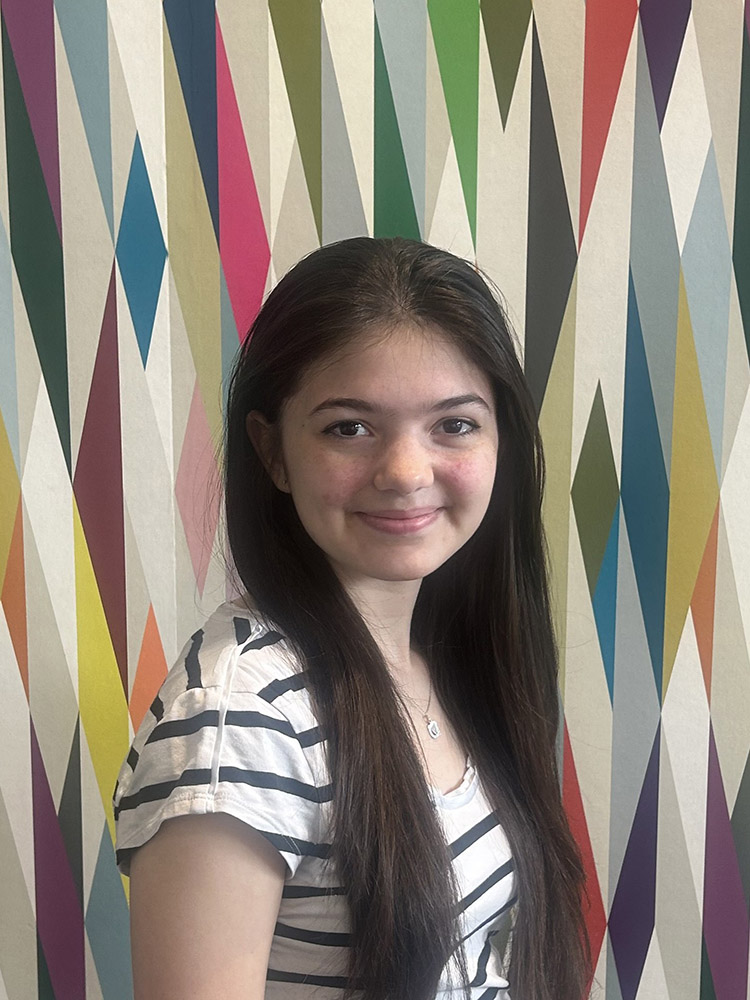 Student Ambassador Claire Higginbotham stands in front of a colorfully painted geometric pattern.