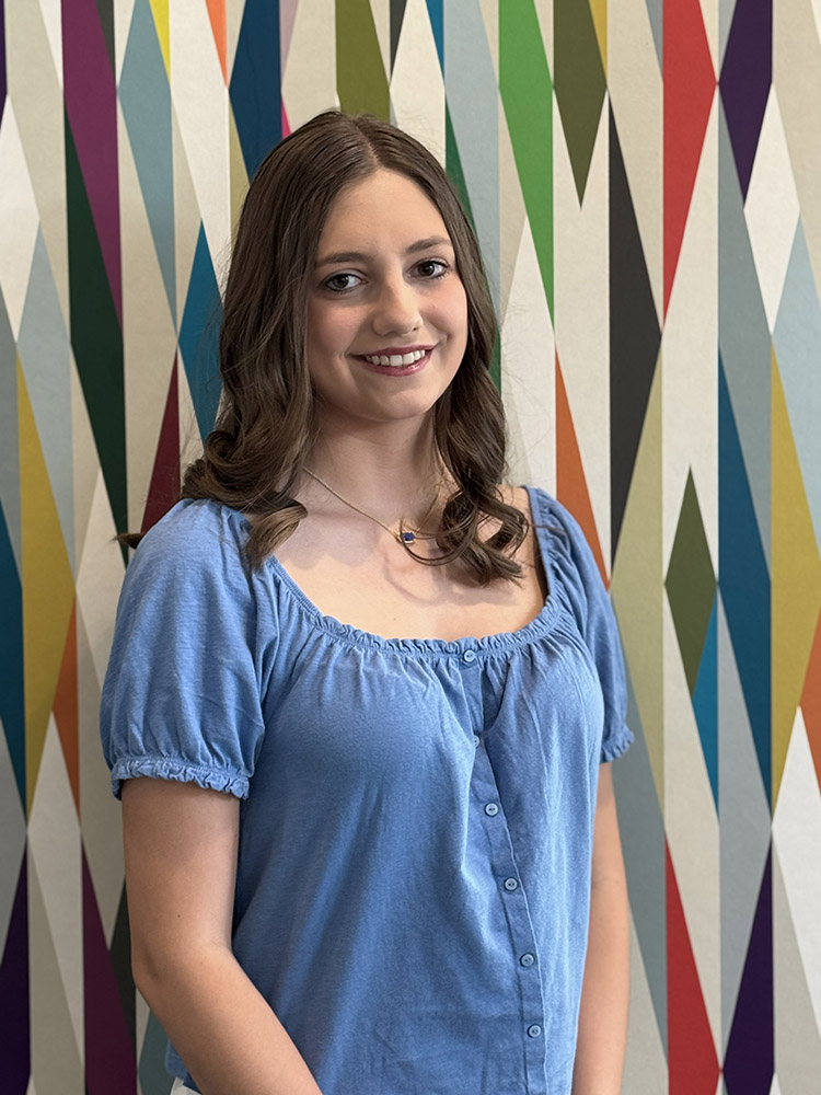 Student Ambassador Emma Singleton stands in front of a colorfully painted geometric pattern.