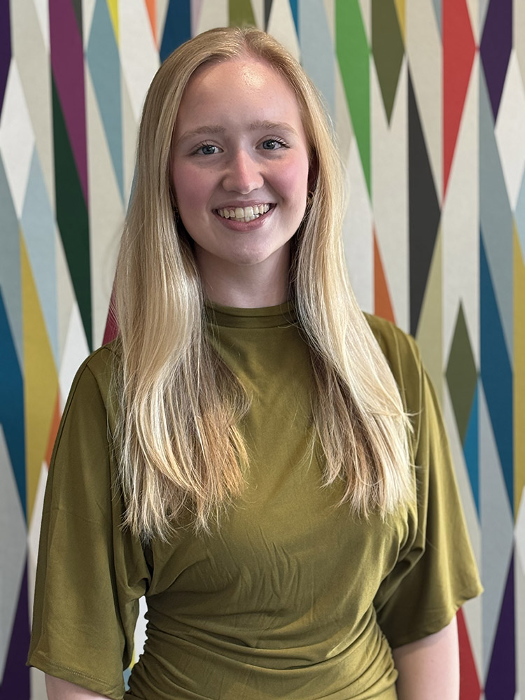 Student Ambassador Kennedy Hamilton stands in front of a colorfully painted geometric pattern.