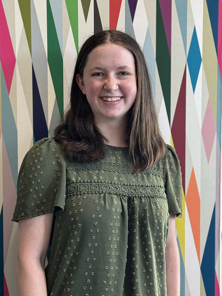 Student Ambassador Sarah Deale stands in front of a colorfully painted geometric pattern.