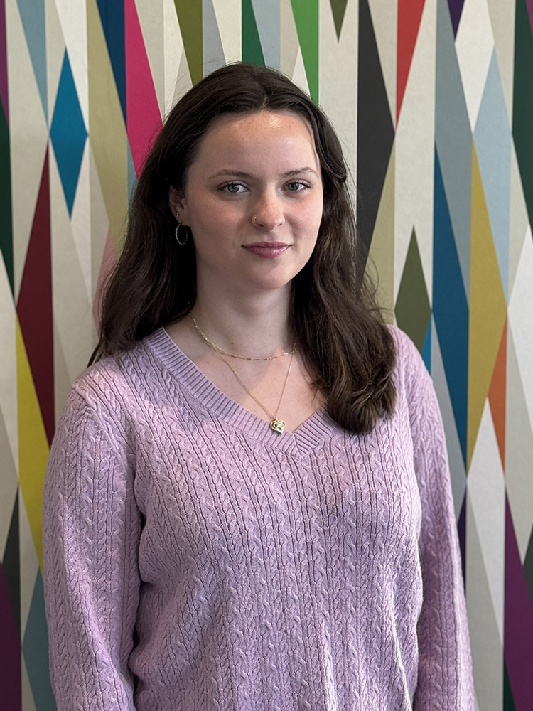 Student Ambassador Trinity Van Meter stands in front of a colorfully painted geometric pattern.