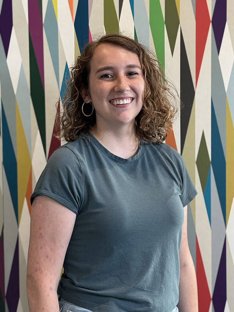 Peer Mentor Aubrey Colbert stands in front of a colorfully painted geometric pattern.