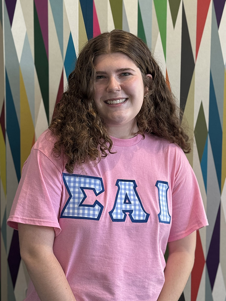 Peer Mentor Claire Martin stands in front of a colorfully painted geometric pattern.