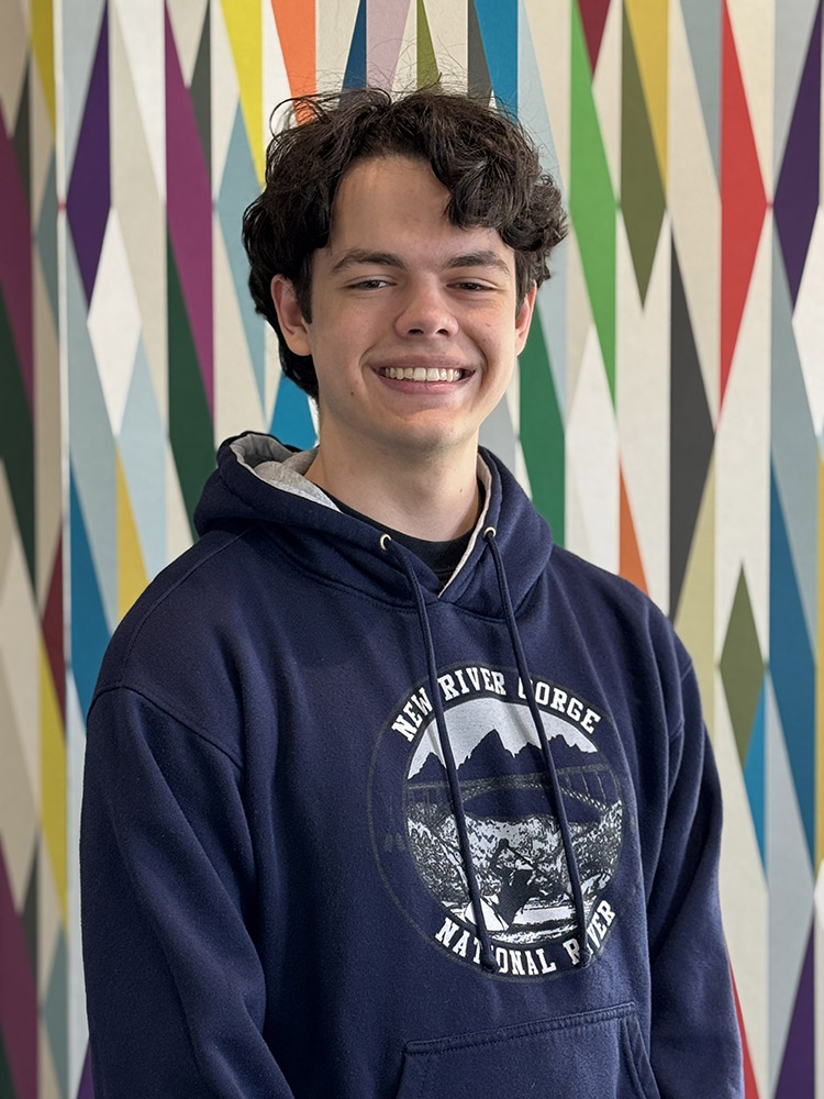 Peer Mentor Josh Braun stands in front of a colorfully painted geometric pattern.