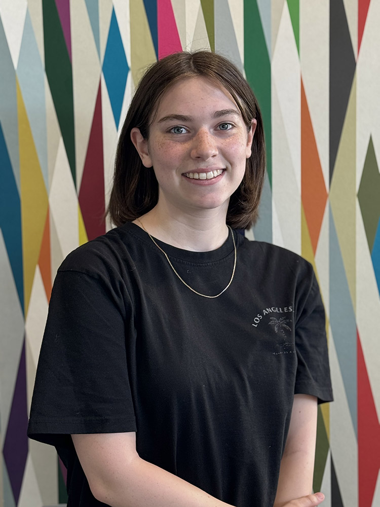 Peer Mentor Katie Skiles stands in front of a colorfully painted geometric pattern.