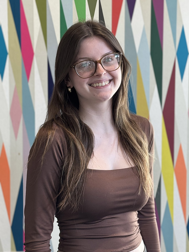 Peer Mentor Kenzie Rose stands in front of a colorfully painted geometric pattern.