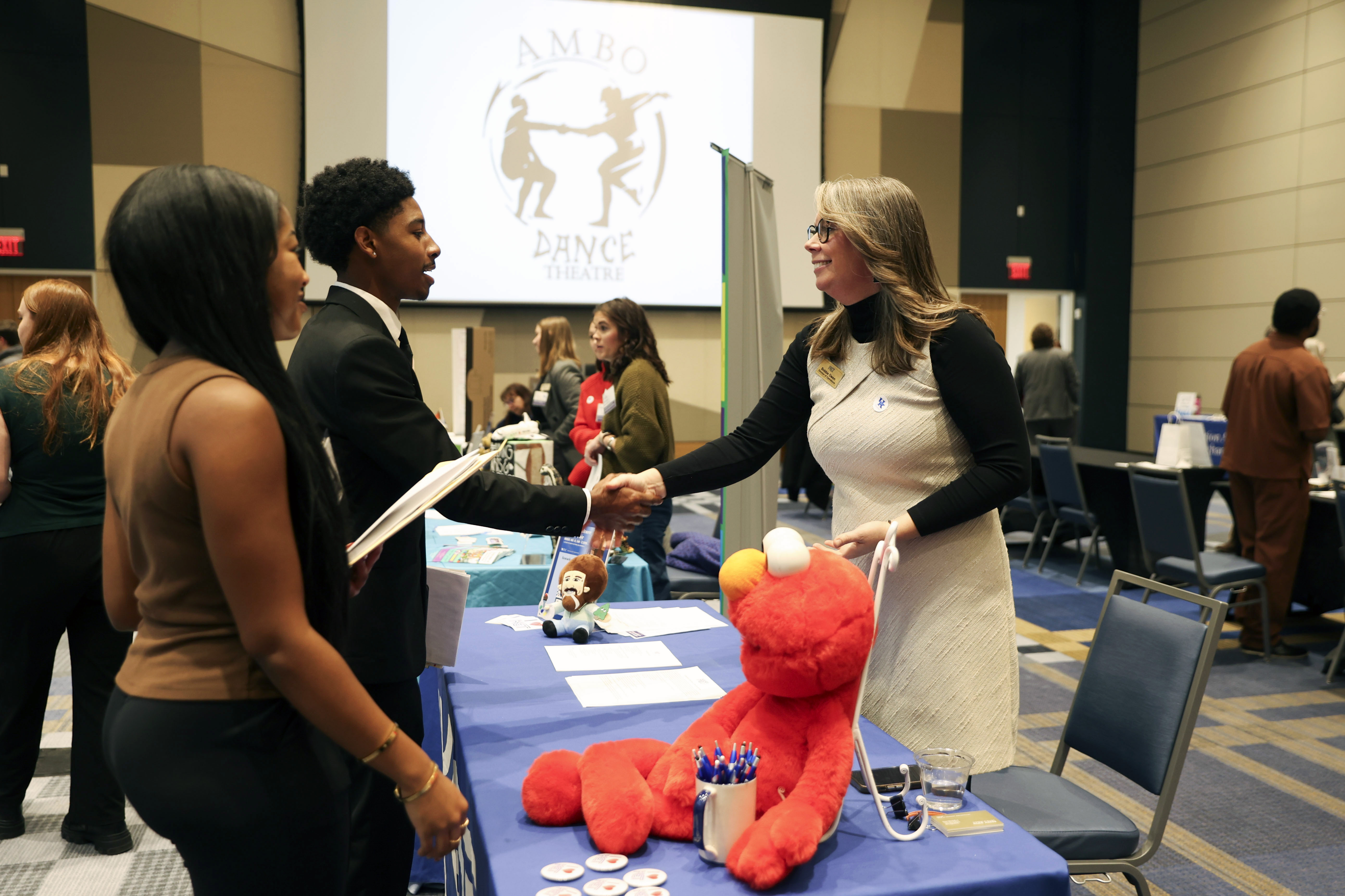 people shaking hands across table with elmo plush in foreground