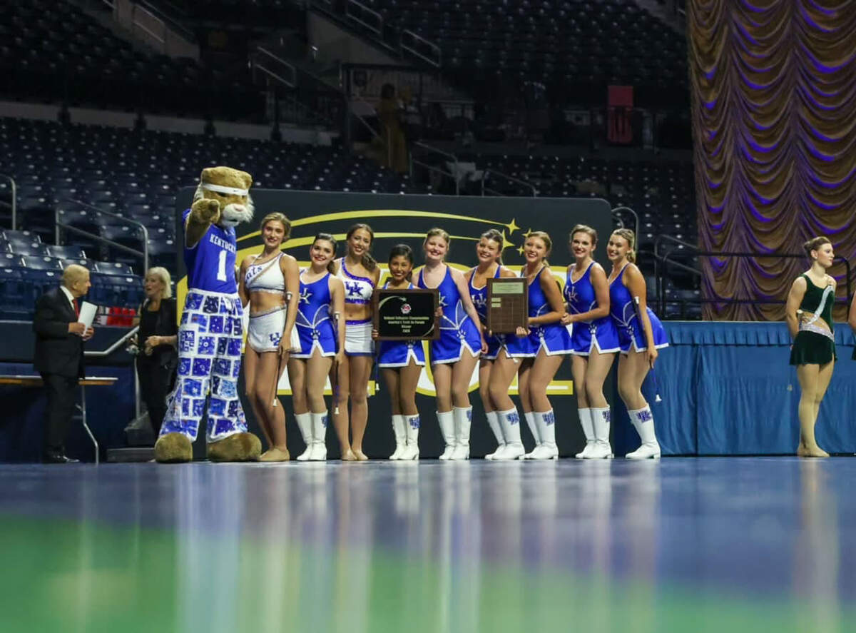 Nine twirlers in UK blue uniforms stand with the UK Wildcat and post with coach Donna Daniels in front of a crowd