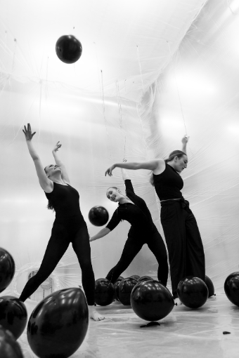 Black and white images of three dancers making various shapes with their bodies while dark balloons float around them.