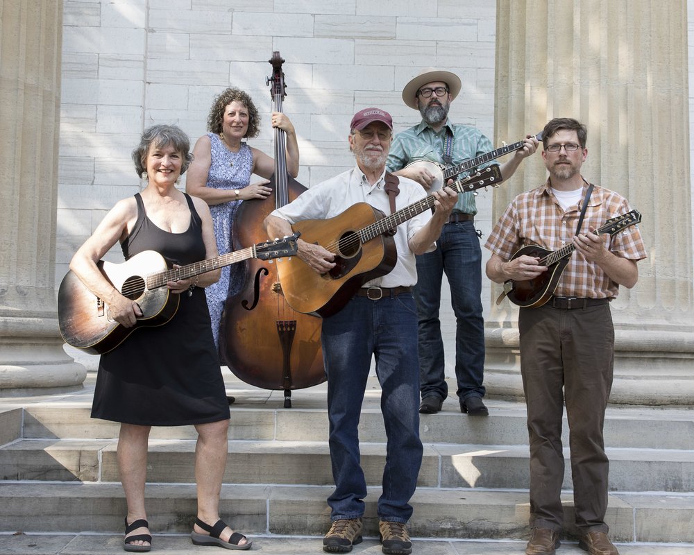 The five members of Kentucky Wild Horse gathered with their instruments on historic stone steps with large roman columns behind them.