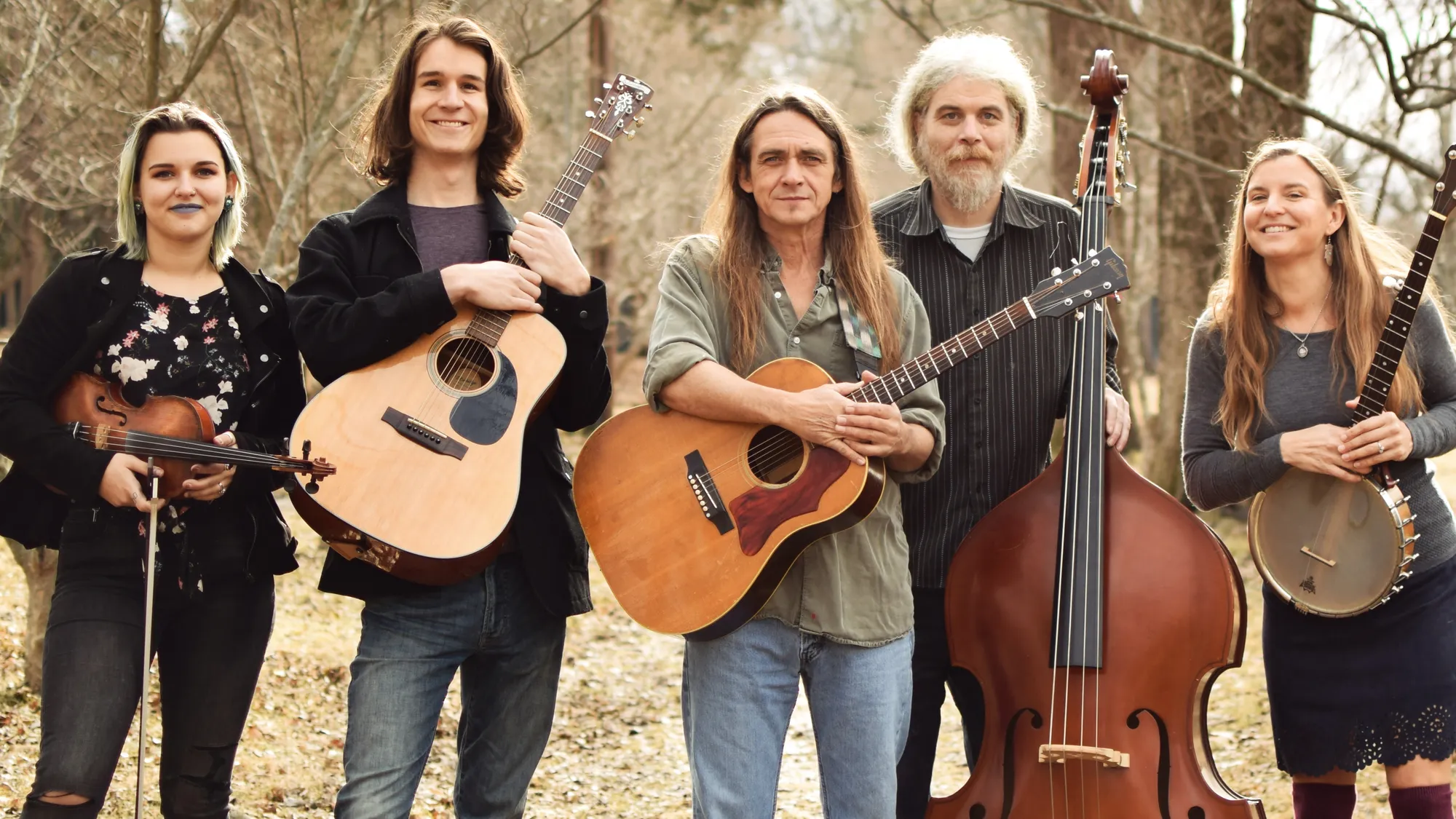 The band Zoey Speaks lined up with their instruments in an autumn forest. From left to right: Zoey Barrett, Arlo Barnette, Mitch Barrett, Owen Reynolds, and Carla Gover.