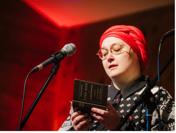 Portrait of Erin Fulton with a red head wrap singing into a mic.