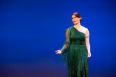 Portrait of Lydia Rufin against a vivid blue background, singing on stage in a green dress.