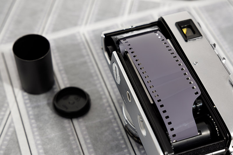 An open film camer lays face down with the back open and a new roll of film loaded in. The empty film tube sits open nearby.