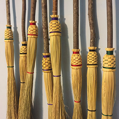 A closeup on several brooms with colorful woven sections covering the attachment of the bristle with the handle.