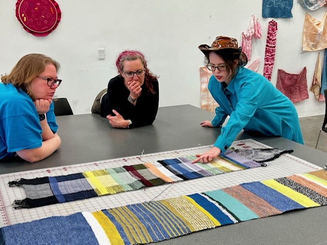 Several people gather around a project laid out on a cutting mat while one points out a proposed change.