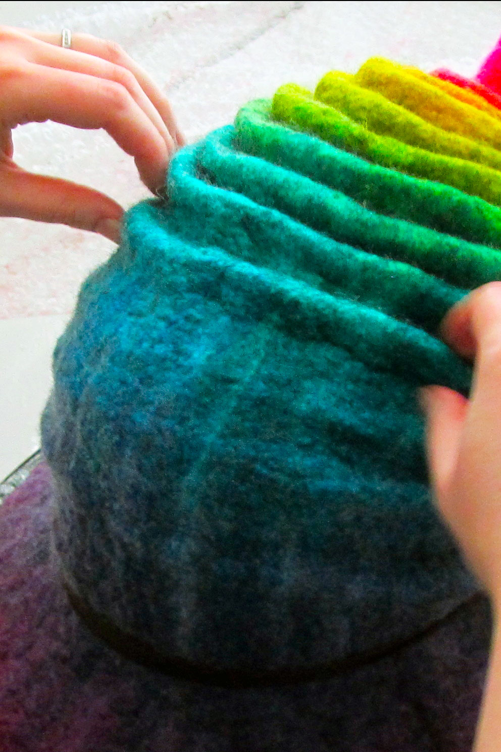 A damp rainbow colored witch hat is being scrunched and pleated artfully towards the brim.