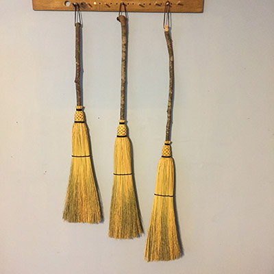Three rustic brooms of increasing length hanging from pegs on the wall.