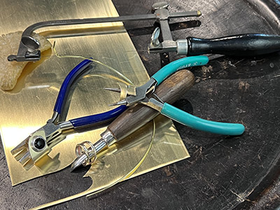 Pieces of brass, pliers, and other jewelry making tools on a workbench.