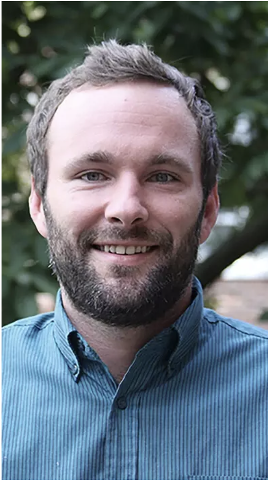 Headshot of Paul Rodgers taken outdoors in front of trees, Paul wears a blue button down.