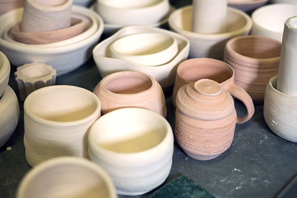 An assortment of student bisque fired and partially glazed pottery in progress.