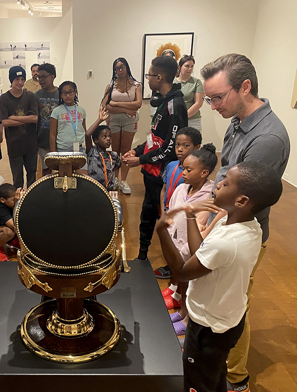 Dan Solberg (right, wearing gray polo) stands with several children and their families while examining a sculptural piece in the museum.