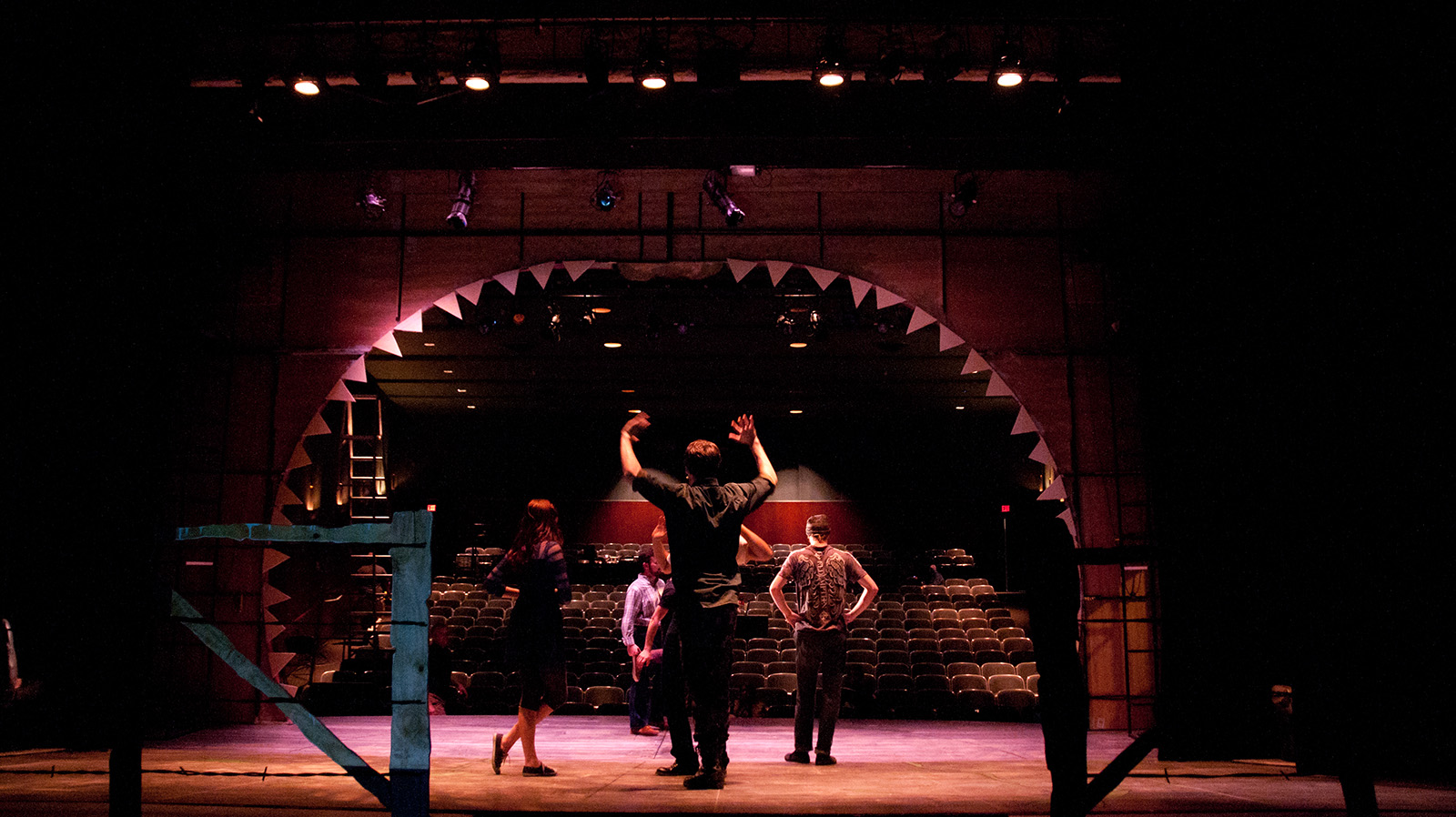 From back stage looking out into an empty audience, student stage crew works on the set and lighting in preparation for a show.