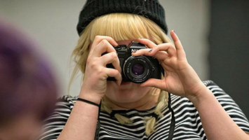 A student with a retro camera held up to their face to take a photograph.