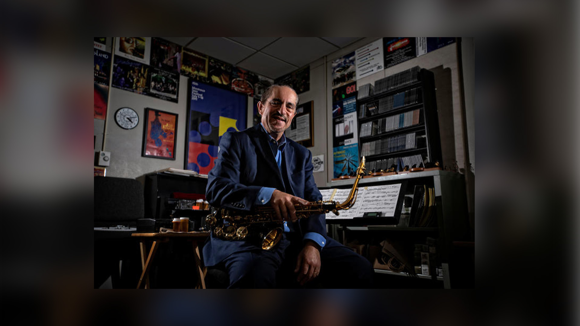 Image of Miles Osland seated, in his studio, holding saxophone.