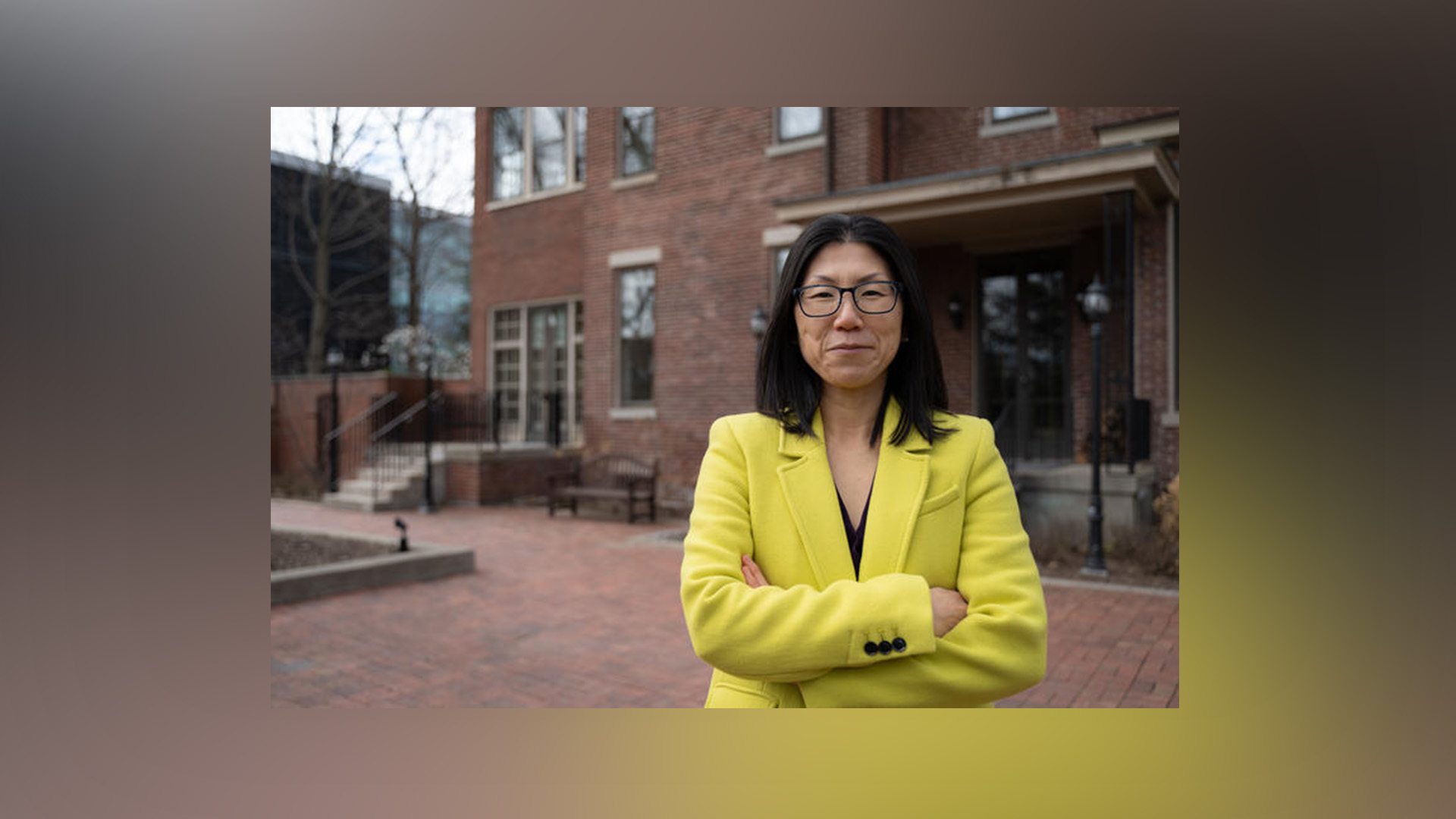 Image of Dr. Yuha Jung wearing yellow blazer, standing outside in front of brick building.