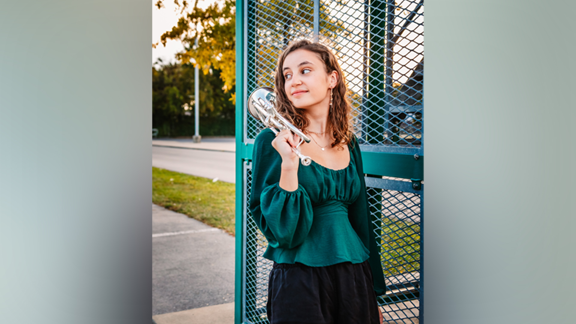 Image of Adrianna Dick wearing a teal shirt and black pants, outdoors with her trumpet