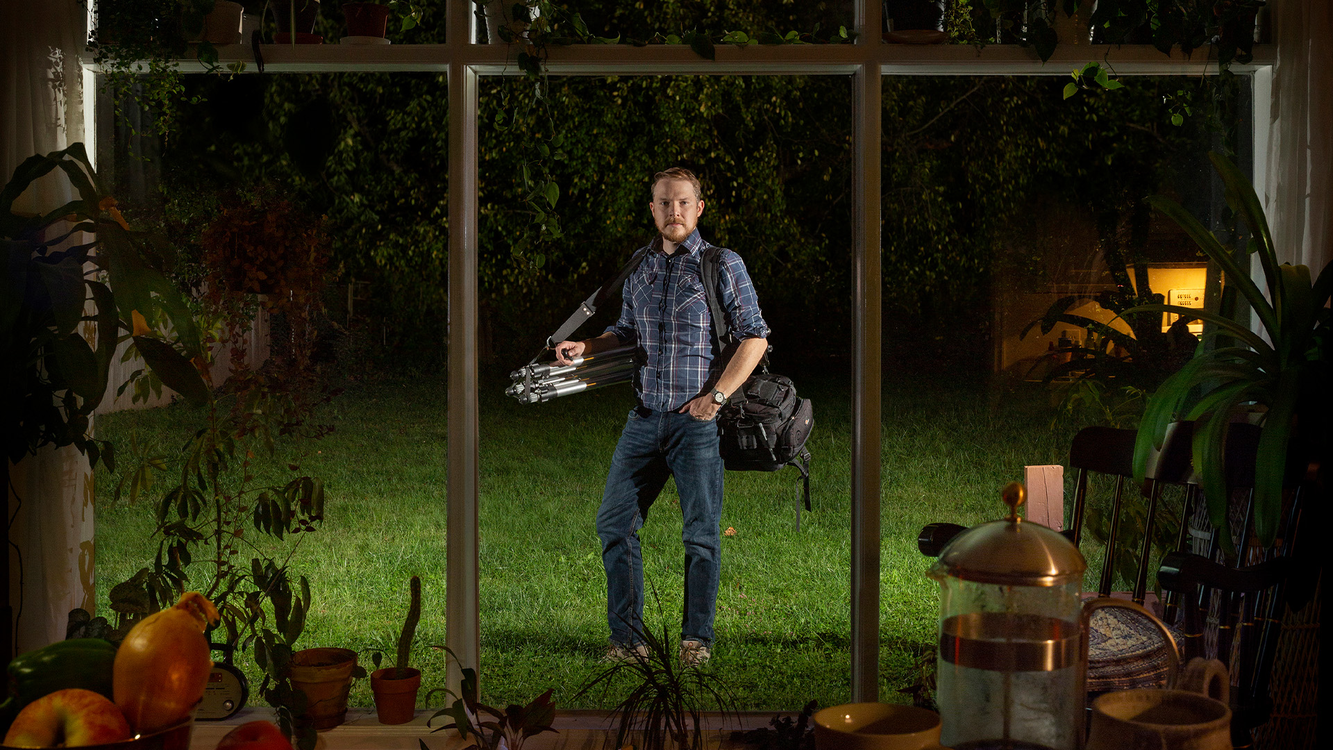 Self portrait photograph of Rob Southard holding photography equipment, in backyard, looking through picture window, 