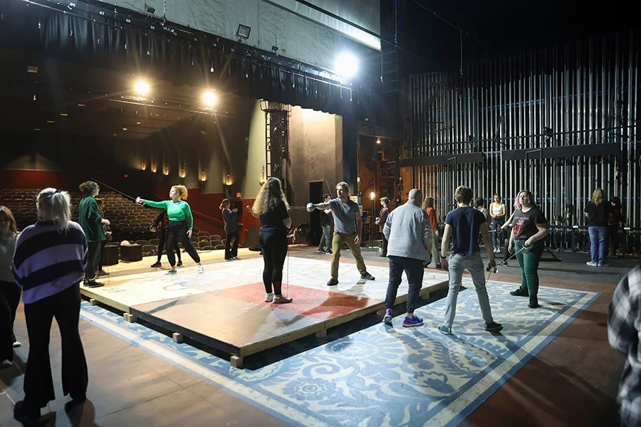 Back stage shot of many students and instructors learning and practicing swordplay in the Guignol Theatre.