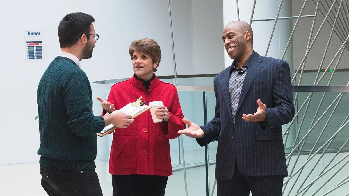 Three people talking in front of sculpture