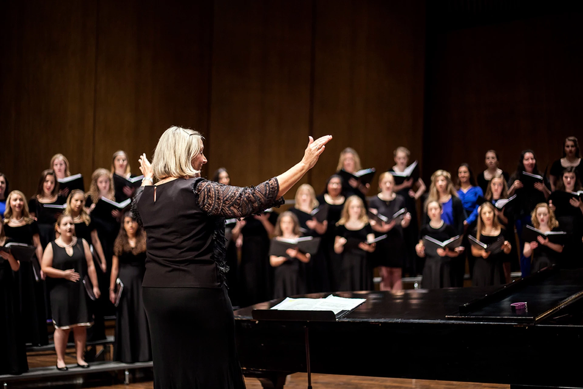 People on stage singing, conductor in front