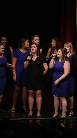 Members of Paws and Listen onstage at the Singletary Center wearing blue and black dresses
