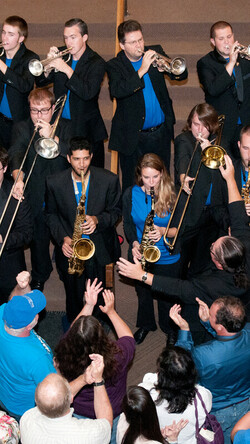 Image of Jazz Studies members on the stairs of the Singletary Center main lobby wearing blue UK polos and holding instruments