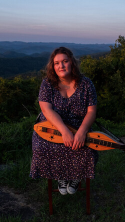 Image of Sarah Kate Morgan seated outdoors against a backdrop of the Appalachian mountains with a dulcimer in her lap.